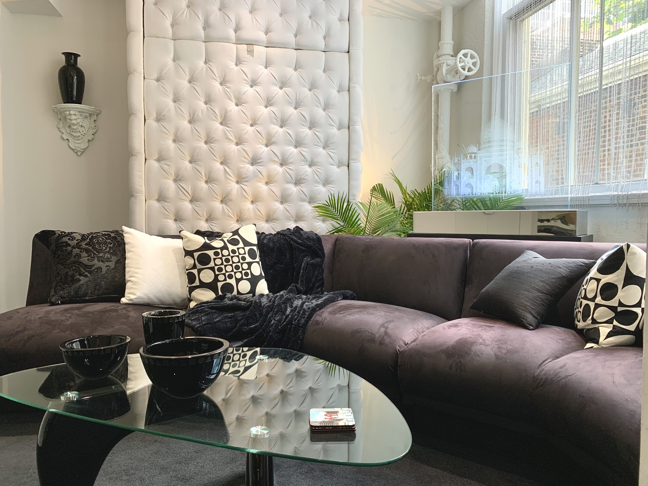 Photo of a grey plush couch and glass coffee table with ceramic bowls. Behind the couch is a custom glass-etched panel featuring the Taj Mahal.